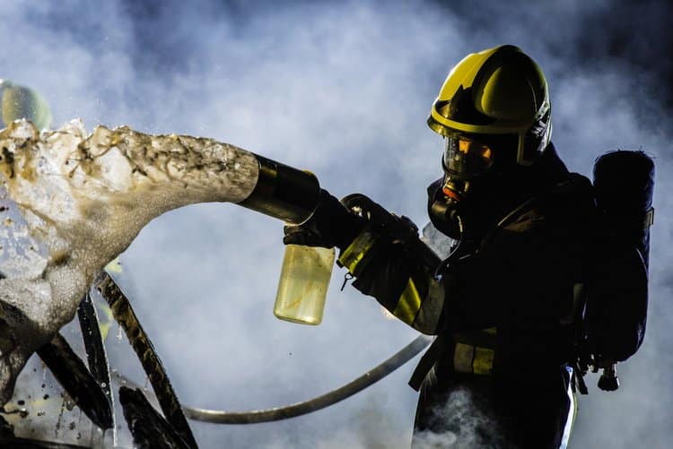 Close-up photo of a firefighter in full gear extinguishing a fire with foam.